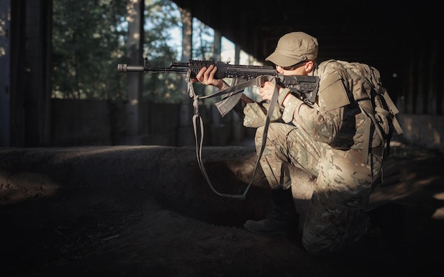 写真 戦術的な黒い眼鏡をかけたカモフラージュの灰色のユニフォームと、許可された大きな建物の内部を遠くに向けて機関銃を手にした帽子をかぶった自国の男性兵士の擁護者