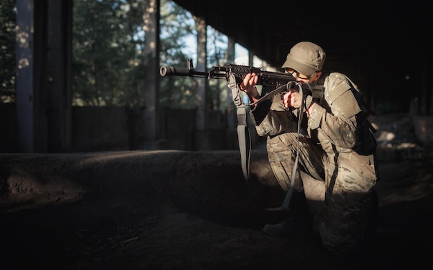 写真 戦術的な黒い眼鏡をかけたカモフラージュの灰色のユニフォームと、許可された大きな建物の内部を遠くに向けて機関銃を手にした帽子をかぶった自国の男性兵士の擁護者