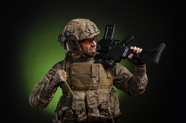 A male soldier in military clothes with a weapon on a dark\
background