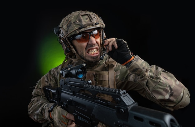 Мужчина-солдат в военной одежде с оружием на темном фоне