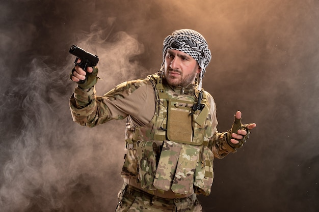 Male soldier in military uniform holding gun on dark smoky wall