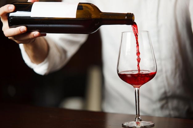 Male sommelier pouring red wine into longstemmed wineglasses