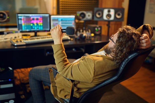 Male sound engineer at mixing consol, back view, recording studio interior on background. Synthesizer and audio mixer, musician workplace