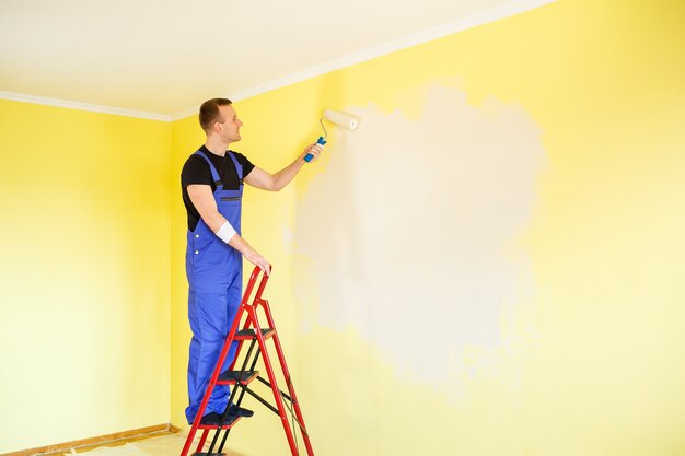 Male specialist paints the wall with paint indoors, repair concept