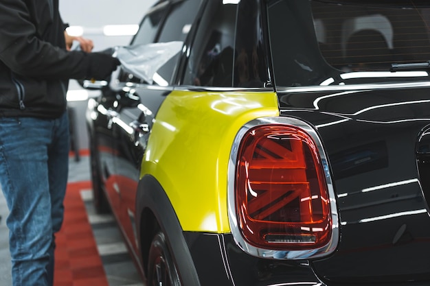 Foto uno specialista maschile avvolge il retro di un'auto nera con un foglio adesivo giallo neon o un'auto con riprese in primo piano