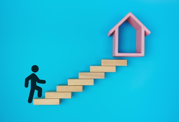 Male stickman climbing the ladders towards home formed by wooden blocks on a blue background