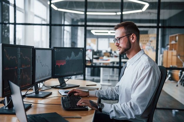 Male stockbroker in formal clothes works in the office with financial market.