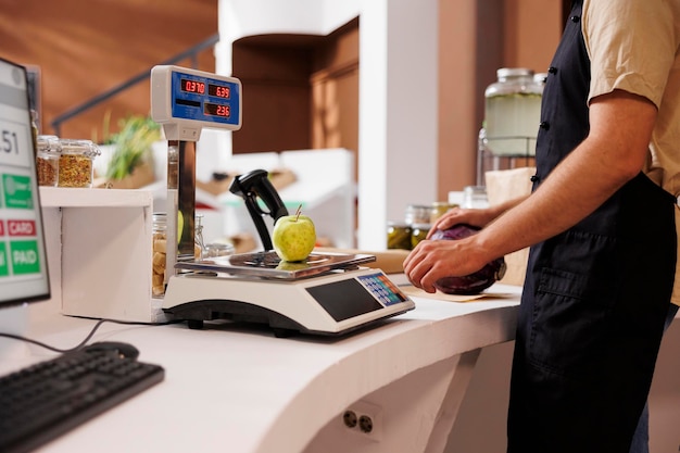 Photo male store worker monitoring a green apple that is on weight scale showing the values and readings caucasian salesman measuring locally grown produce at checkout counter