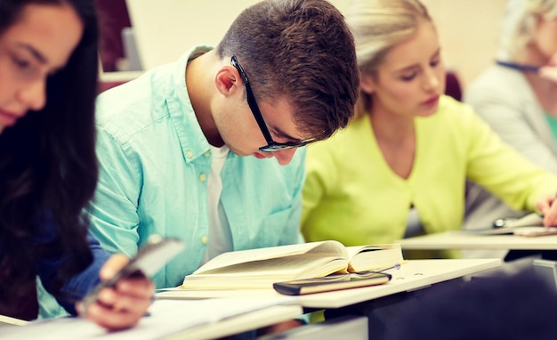 Foto studente maschio con gli occhiali che legge un libro in una lezione