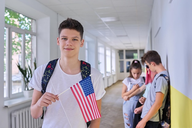 Male student teenager with USA flag inside college, group of students background. United States of America, education and youth, patriotism people concept