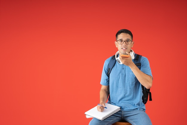 Male student with glasses talking on speaker phone holding a notebook and pencil