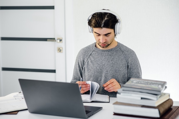 Male student with headphones on head eating sandwich and using laptop