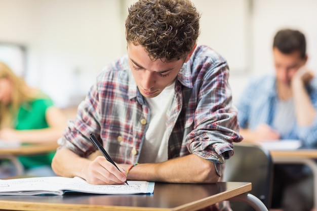 Studente maschio con gli altri scrivere note in aula