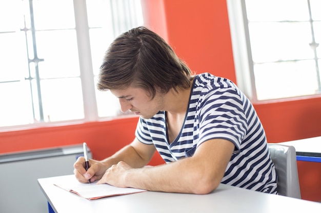 男性の学生が教室でノートを書く