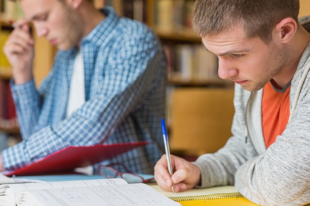 male students writing notes at library desk