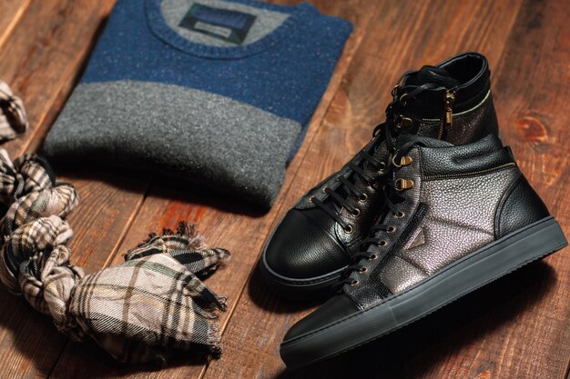 Male stylish boots pullover and scarf on wooden desk.