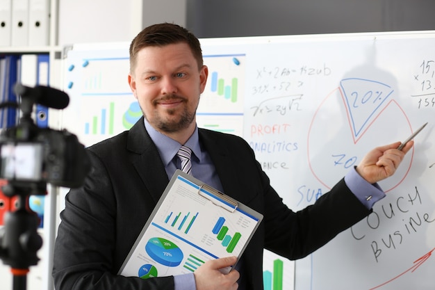 Male in suit and tie show stats graph pad against whiteboard