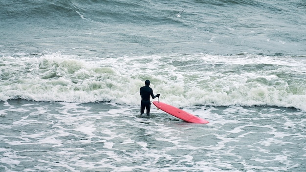 Male surfer in black swimsuit in ocean with red surfboard waiting for big wave