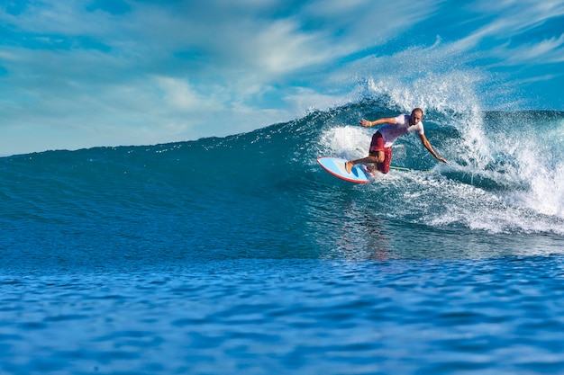 Surfista maschio su un'onda blu al giorno pieno di sole