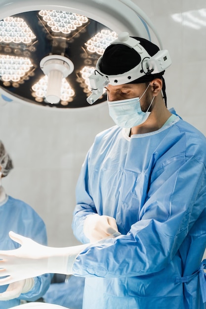 男性外科医は手術用手袋を着用し、手術前に消毒します ヘッドライトを持つ外科医は診療所で手術の準備をしています