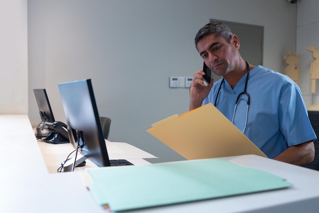 Photo male surgeon talking on mobile phone while looking at medical report at desk