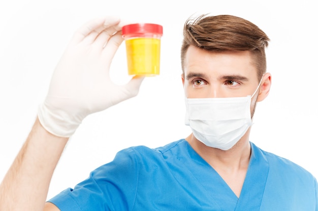 白い背景で隔離の尿サンプルのボトルを保持しているマスクを持つ男性外科医