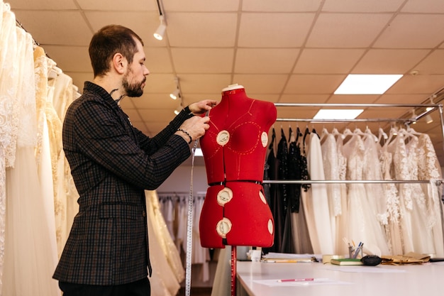男性の仕立て屋または針子がファッションデザインスタジオで巻尺で布のパターンのマネキン測定を行う女性デザイナーがワークショップのドレスメイキングと縫製のコンセプトでダミーを使用