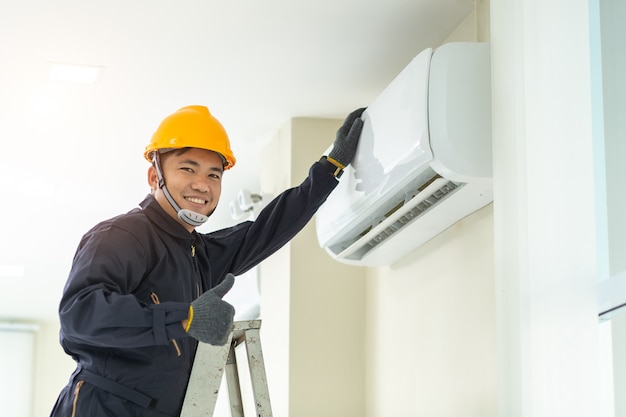 Male technician repairing air conditioner safety uniform indoors. 