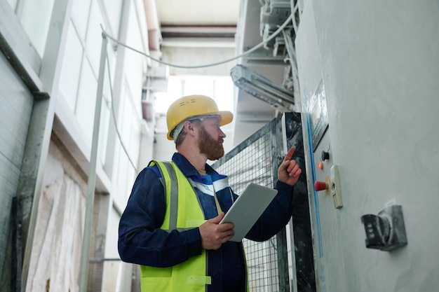 Male technician with tablet switching production equipment in factory