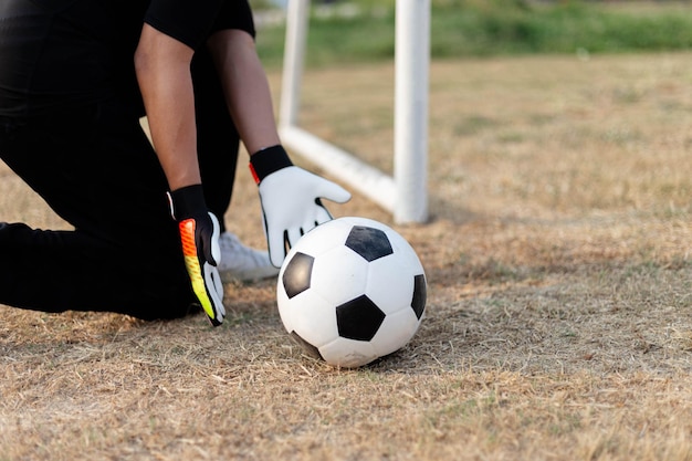 黒の衣装とサッカーを保持しているカラフルな手袋を身に着けている男性の10代のゴールキーパー