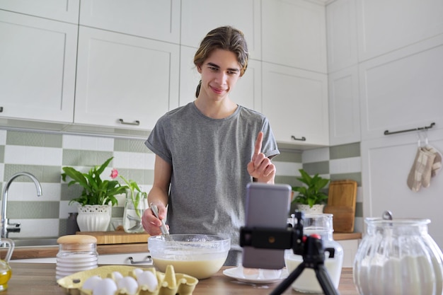 Male teenager cooking pancakes talking on video communication on smartphone