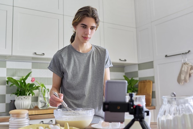 Male teenager learns to cook pancakes watching video recipe on smartphone