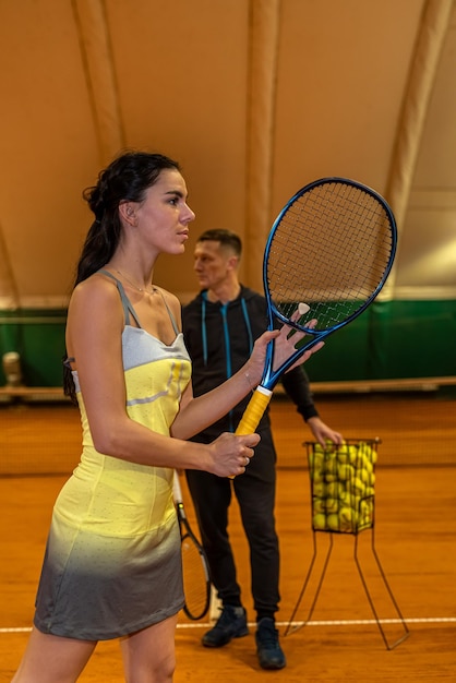남성 테니스 코치가 여성 고객에게 코트에서 봉사하는 방법을 보여줍니다.