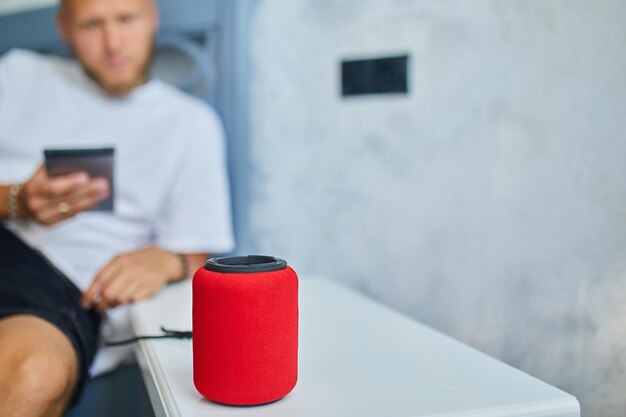 Male testing talking smart wireless speaker man controlling home devices with a voice commands sitting on sofa at home Concept of smart home