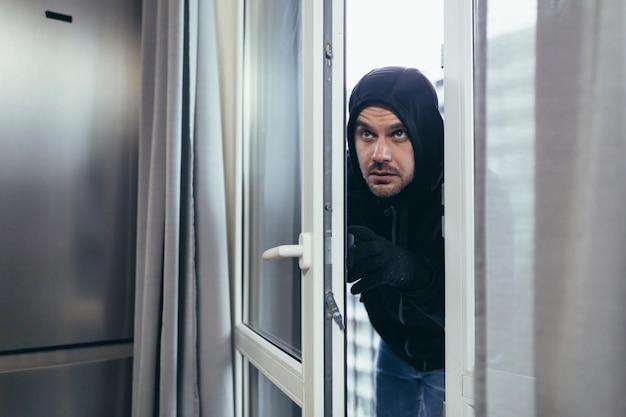 Male thief in black clothes trying to break the door lock in the house