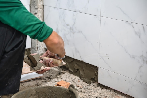 Male tiler using trowel laying marble tile with cement in bathroom Housing development Interior improvement renovation