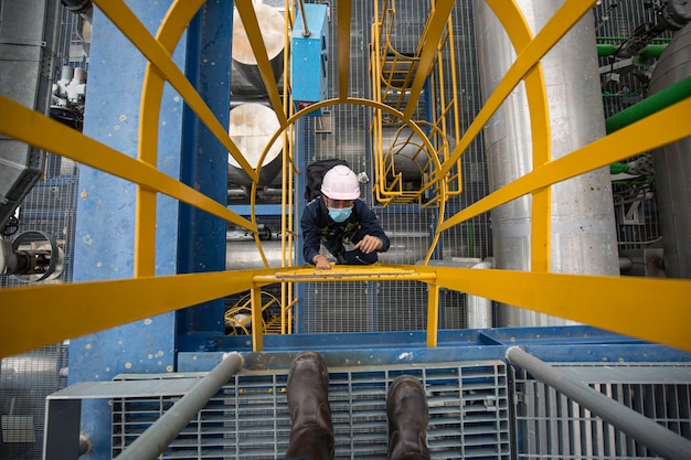 Vista dall'alto maschio salire la sottostazione di trasmissione elettrica e centrale elettrica della conduttura di ispezione dell'impalcatura delle scale