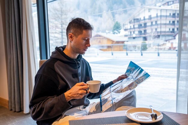 リゾートカフェでコーヒーを飲みながらスキーマップを分析する男性観光客