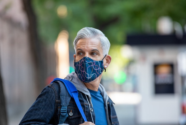 Male tourist in mask and with backpack walking along street in Madrid and enjoying view of city