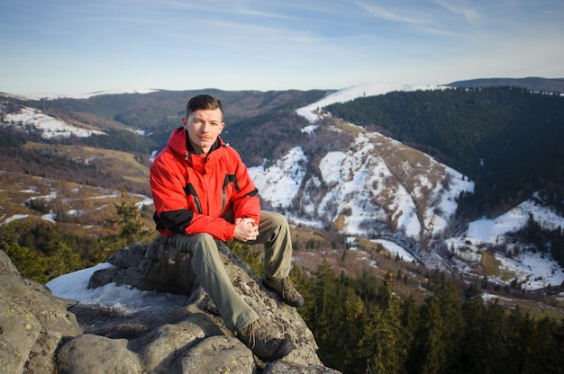 Мужской турист сидит на скале на вершине горы