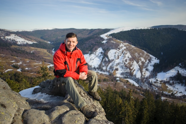 Turista maschio che si siede sulla roccia in cima alla montagna