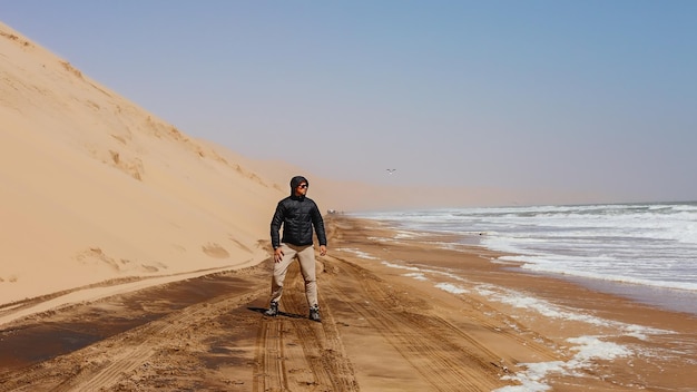 A male tourist wearing a black jacket is looking at the ocean. Sandwich Harbor. Namibia.