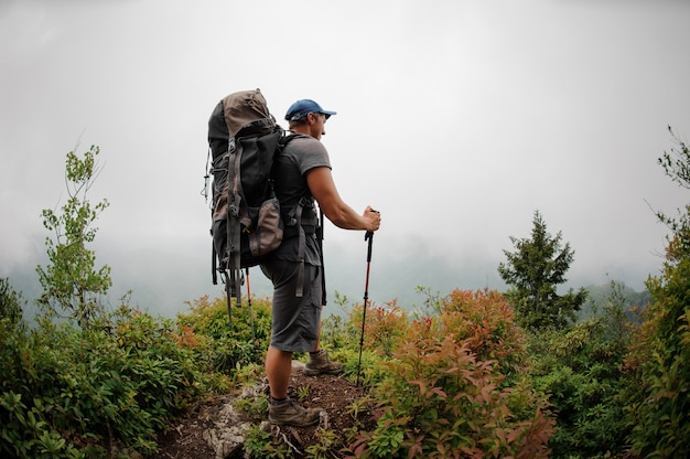 Male tourist with backpack standing among bushes