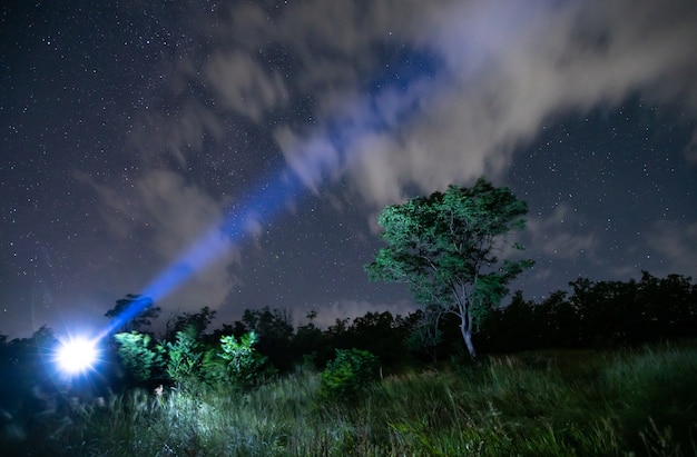 Male tourist with flashlight on head, starry sky in woods.