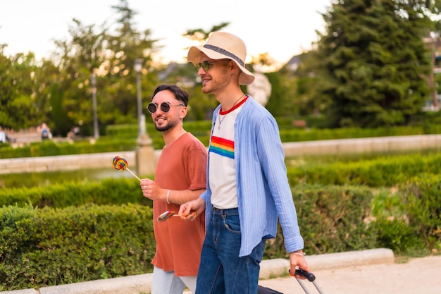 Male tourists gay boyfriends with a suitcase in the park on sunset in the city visiting the city for the pride festival lgbt concept