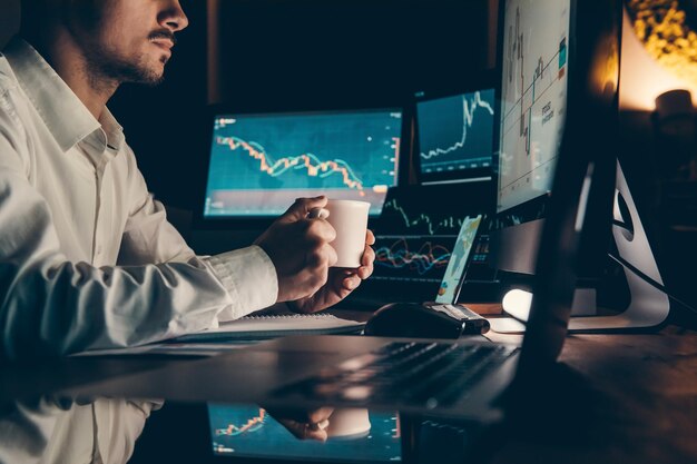 Male trader holding coffee cup while analyzing stock market data on multiple computers at office