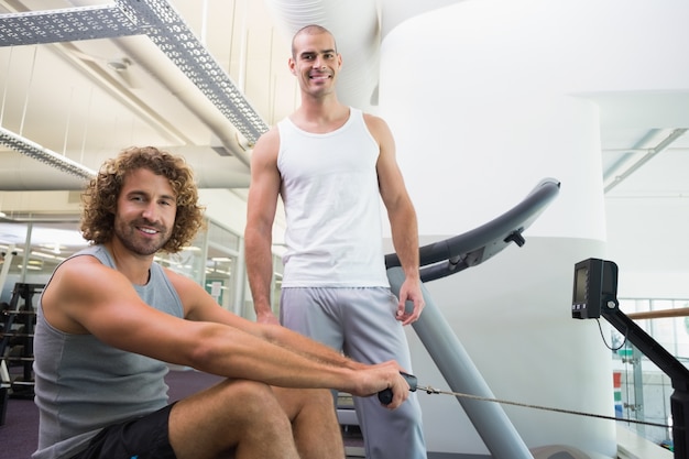 Male trainer assisting man on fitness machine at gym