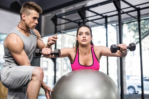 Male trainer assisting woman lifting dumbbells at  gym