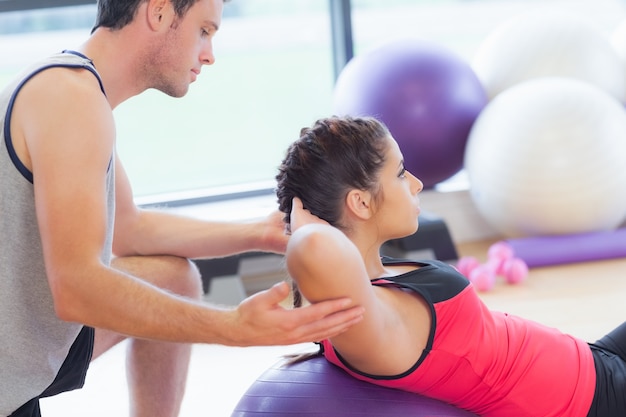 Male trainer helping woman do crunches  on fitness ball at gym