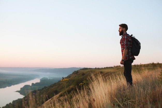 Male traveler admiring sunrise sky over valley with river during trip